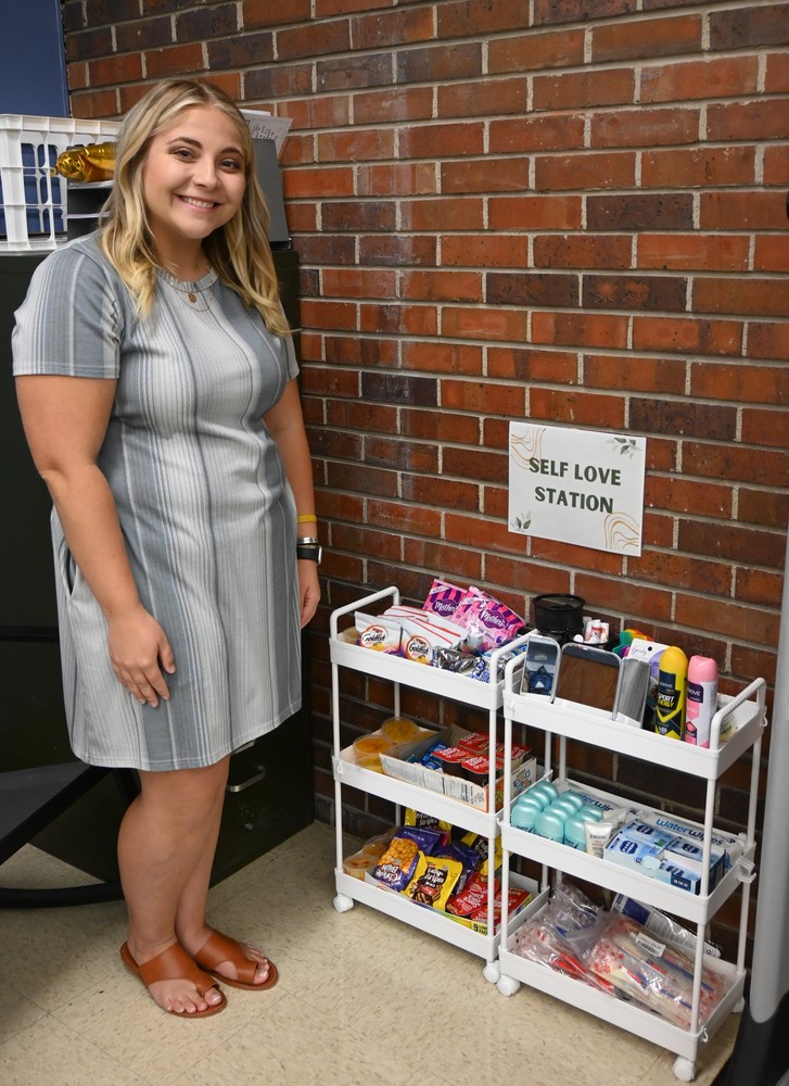 Guthridge fourth grade teacher Allie Jones stands beside  some small shelving units filled with snacks, deoderant and toothbrushes.