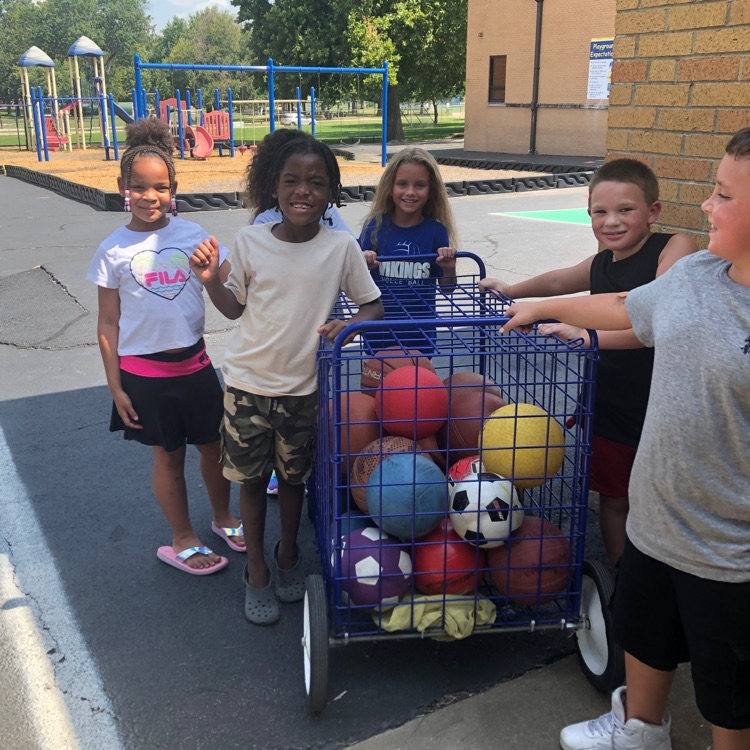 students standing around a large rolling cart full of playground balls  