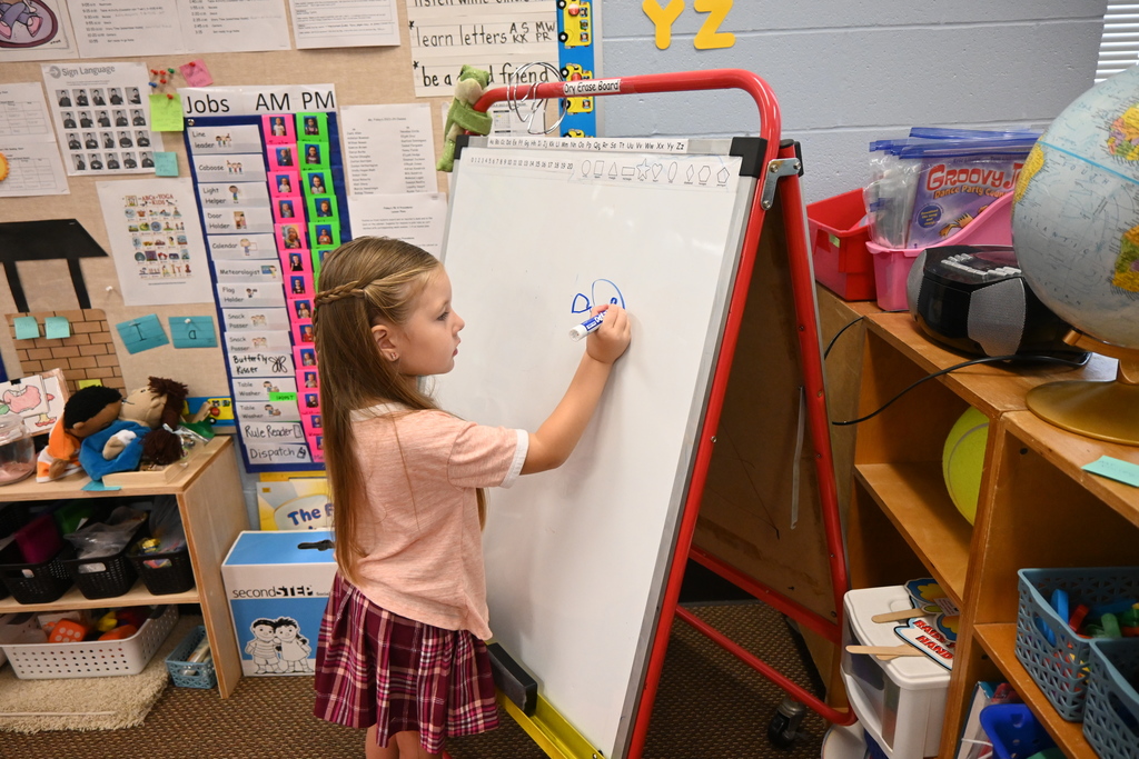 A little girl draws on a whote board easel with a marker.