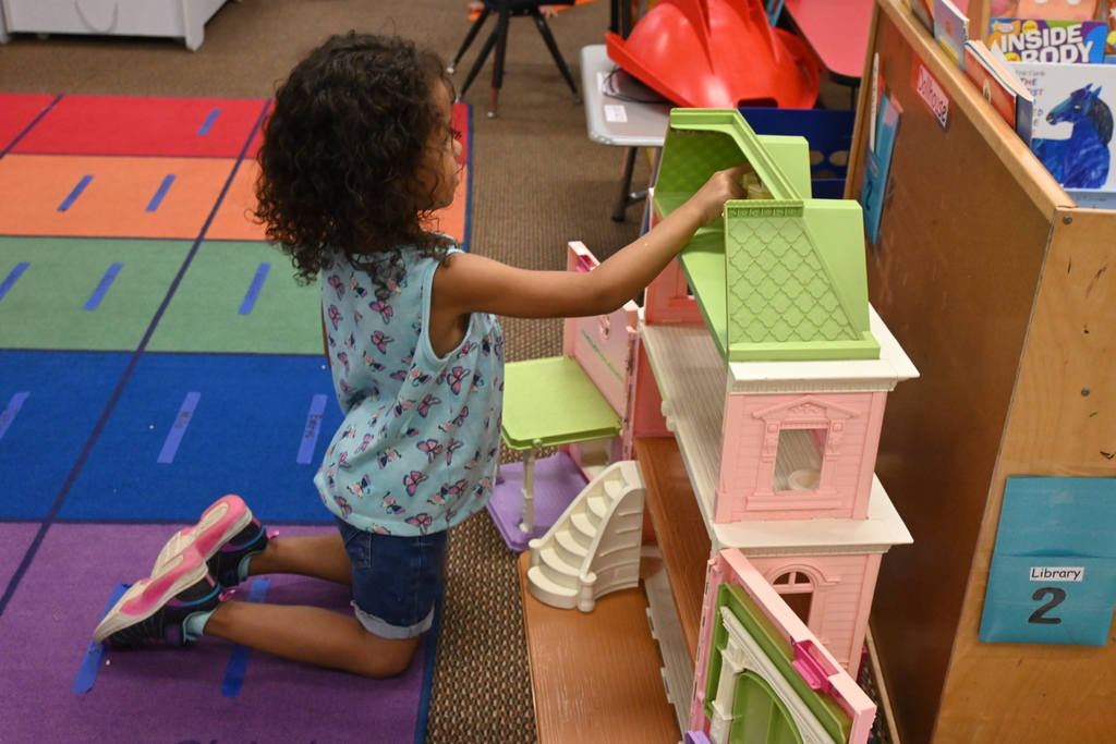 A little girl plays with a doll house.