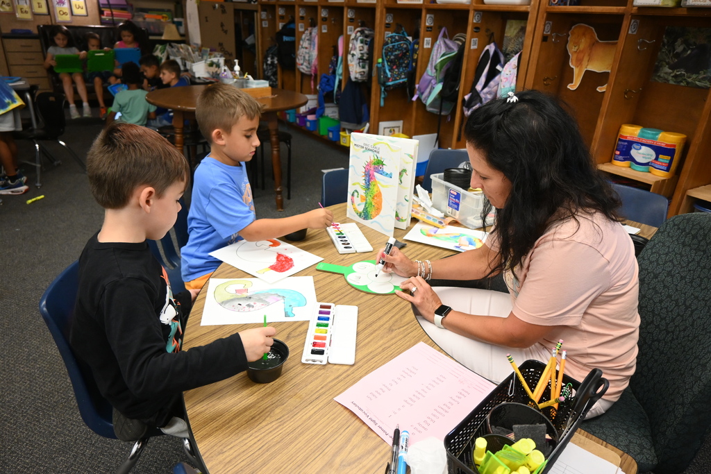 two boys use water colors to paint a seahorse, as Mrs. Hicks tells them the next color to use from her list of words.