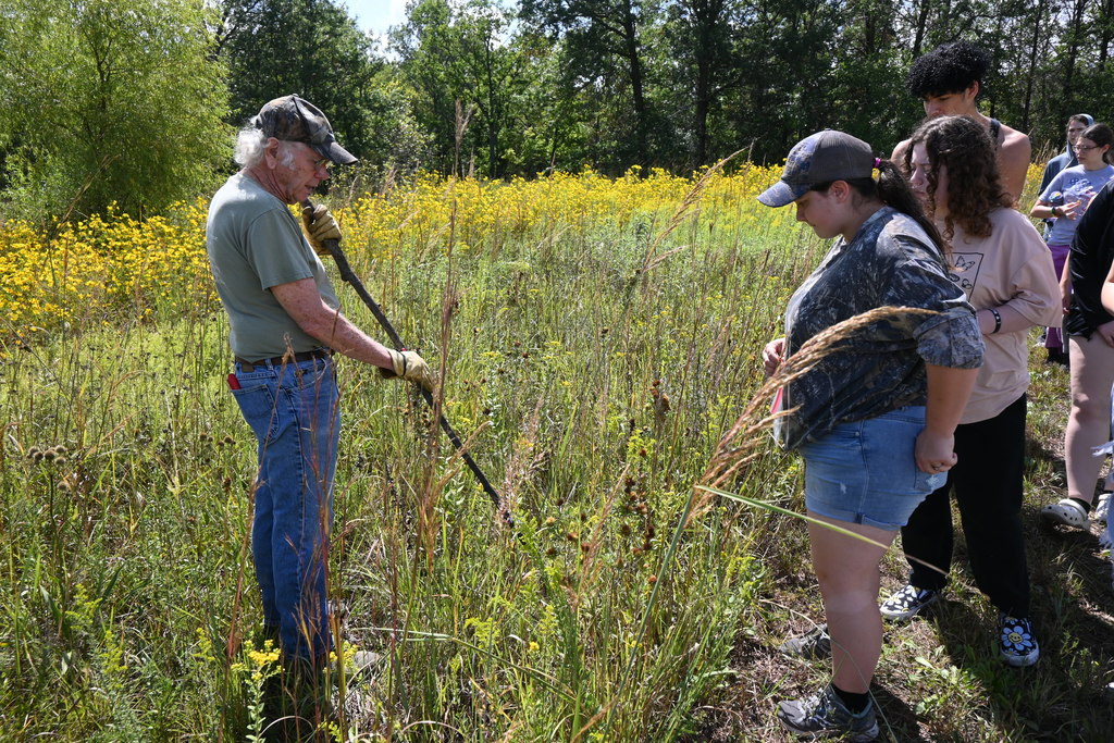 Maz uses his walking stick to point out a plant to students.